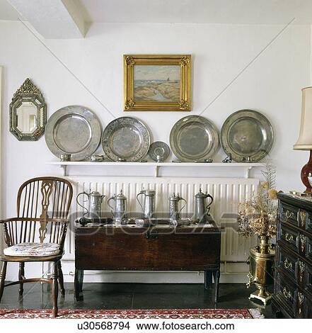 Antique Windsor chair and oak chest with pewter jugs below collection of pewter plates on shelf above radiator View Large Photo Image Picture - Antique Windsor chair and oak chest with pewter jugs below collection of pewter plates on shelf above radiator. Fotosearch