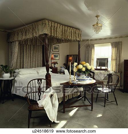 Antique Windsor chairs and gateleg table in country bedroom with fourposter bed with beige drapes and white bedlinen View Large Photo Image Stock Photo - Antique Windsor chairs and gateleg table in country bedroom with fourposter bed with beige drapes and white bedlinen. Fotosearch