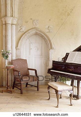 Stock Image - Armchair and grand piano beside Gothic door in country living room with Gothic stone pillar. Fotosearch