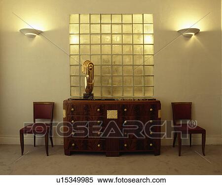 Art Deco sculpture on thirties chest of drawers in front of glass brick wall in white hall with lighted wall-lights View Large Photo Image Stock Photography - Art Deco sculpture on thirties chest of drawers in front of glass brick wall in white hall with lighted wall-lights. Fotosearch