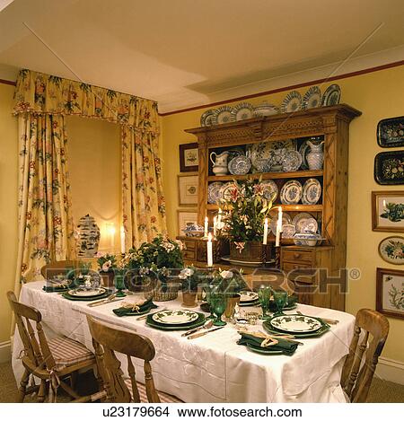 Picture - Baskets of flowers and green plates on white tablecloth in yellow dining room with dresser and yellow floral curtains. Fotosearch