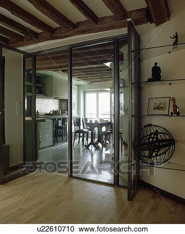 Stock Image - Beamed hall with wooden flooring and modern glass and metal doors to kitchen dining room. Fotosearch