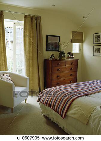 Beige linen curtains and cream tub chair in bedroom with striped throw on bed and antique chest of drawers View Large Photo Image Stock Photography - Beige linen curtains and cream tub chair in bedroom with striped throw on bed and antique chest of drawers. Fotosearch