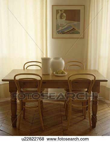 Stock Photo - Bentwood Thonet chairs and white vases on antique pine table in neutral dining room with parquet floor. Fotosearch