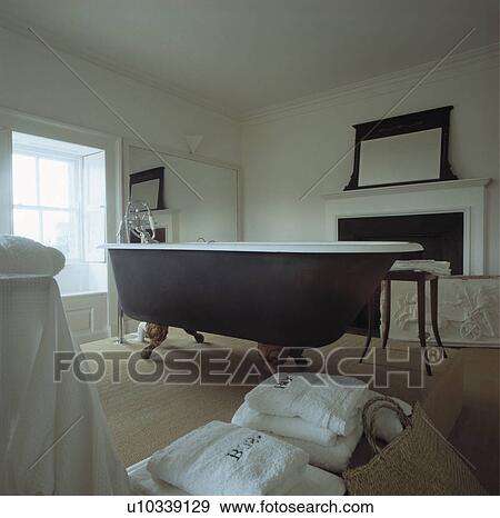 Stock Photo - Black clawfoot bath in white country bathroom with pile of white towels on sisal carpet. Fotosearch
