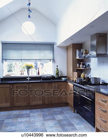 Stock Photograph - Black range oven and grey flooring in modern kitchen with slatted blind above sink. Fotosearch
