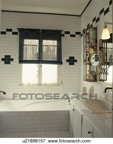 Stock Photo - Black split-cane blind on window above bath in modern white tiled bathroom with black tiling pattern. Fotosearch