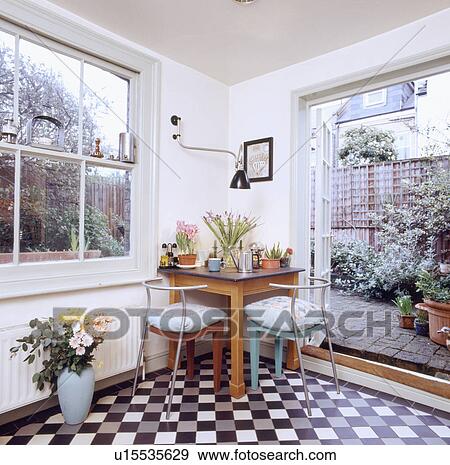Stock Photo - Black & white tiled floor in small dining room extension with wooden table & metal chairs and open patio doors. Fotosearch