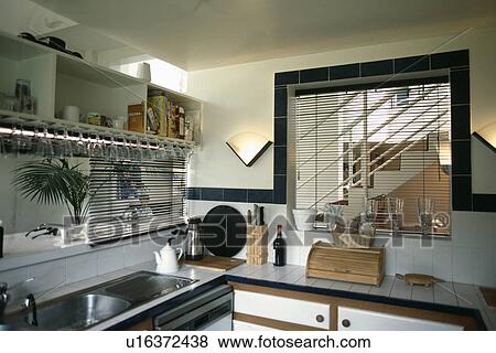 Stock Photo - Blind above double steel sink in small white kitchen with blind on internal window with view of staircase. Fotosearch