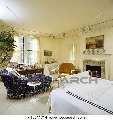 Picture - Blue chaiselongue in cream bedroom cream carpet and picture above fireplace. Fotosearch