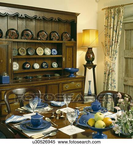 Blue Crockery On Table In Dining Room With Oak Dresser And Lighted