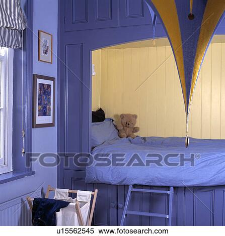 Stock Photography - Blue duvet on bed fitted into alcove with cream panelling in child's blue spacesaving bedroom. Fotosearch