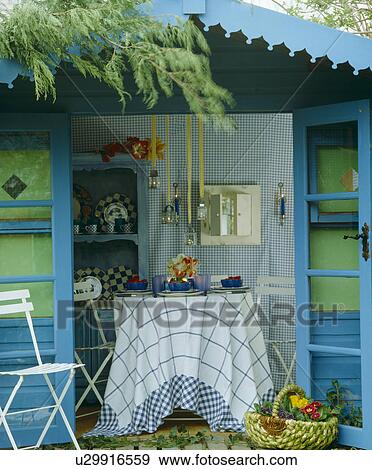 Stock Photo - Blue garden shed with open doors and candle lanterns above dining table with blue and white checked cloth. Fotosearch