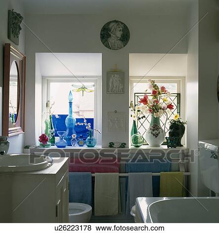 Blue glassware on windowsill of small family bathroom with pastel towels on storage rail View Large Photo Image Stock Photo - Blue glassware on windowsill of small family bathroom with pastel towels on storage rail. Fotosearch