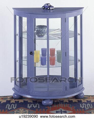 Stock Image - Blue semi circular thirties style cupboard with glass shelves and mirrored back. Fotosearch