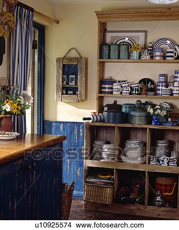 Picture - Blue+white Cornishware on pine shelves above reclaimed wooden cube shelving in kitchen with blue wooden panelling. Fotosearch