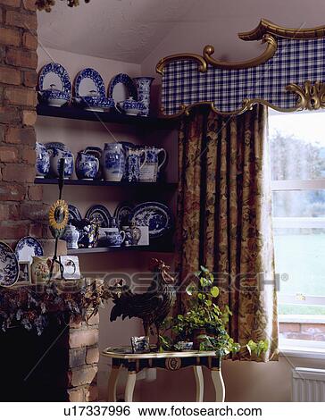 Stock Photograph - Blue+white jugs on shelves beside window with gilt-edged blue+white checked pelmet and floral curtains. Fotosearch