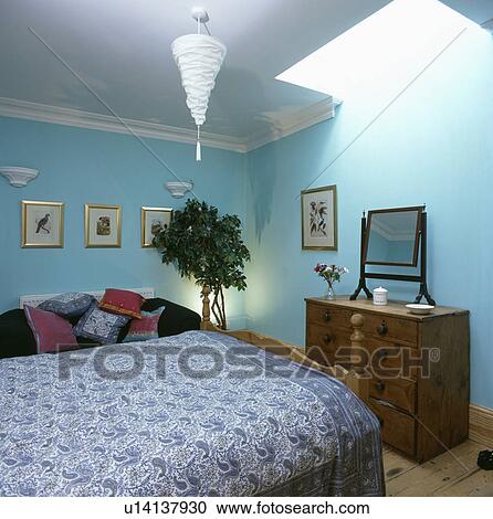 Stock Image - Blue+white Paisley bedcover in pastel turquoise bedroom with mahogany chest of drawers. Fotosearch