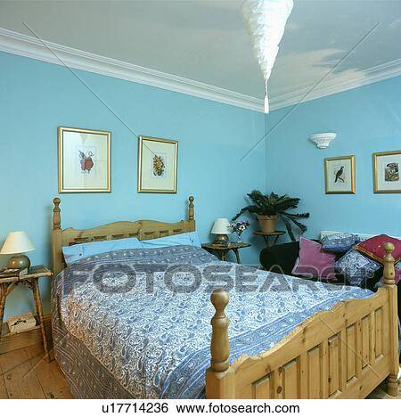 Stock Photograph - Blue+white Paisley bedcover on pine bed in pastel turquoise bedroom. Fotosearch