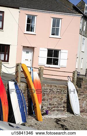 Stock Photograph - Boats on beach below peach cottage with white shutters in Cornish village. Fotosearch