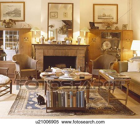 Books on wooden table and Lloyd Loom armchairs in traditional living room View Large Photo Image Stock Photography - Books on wooden table and Lloyd Loom armchairs in traditional living room. Fotosearch