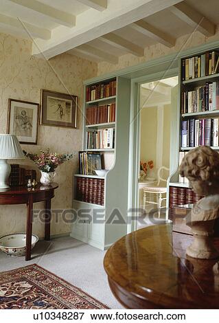Stock Photo - Bookshelves on either side of pastel turquoise doorway in cottage hall with wallpaper and white beamed ceiling. Fotosearch