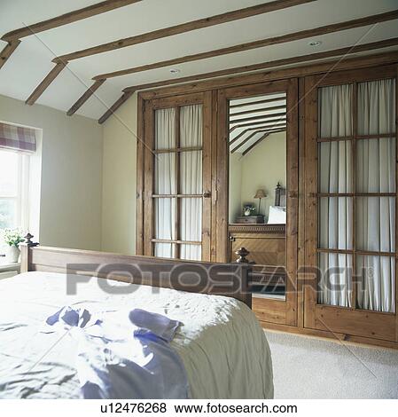 Stock Photo - Built-in cupboards with mirror and glass panelled doors in country bedroom. Fotosearch