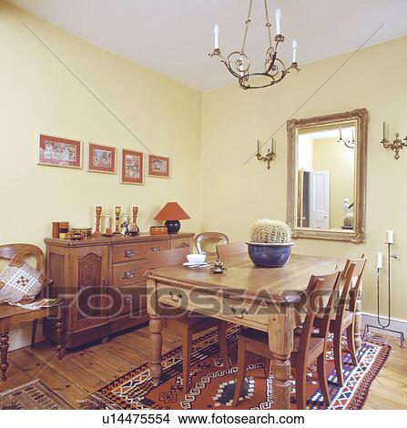 Picture - Cactus on wooden table in pastel yellow dining room with sideboard and patterned rug . Fotosearch
