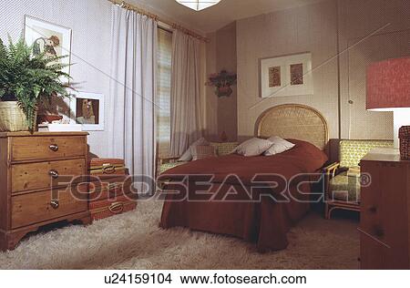 Cane bed with terracotta duvet and vallance in bedroom with cream shagpile rug and pine chest-of-drawers View Large Photo Image Picture - Cane bed with terracotta duvet and vallance in bedroom with cream shagpile rug and pine chest-of-drawers . Fotosearch