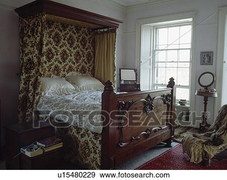 Stock Photo - Carved wooden antique half-tester bed with patterned curtainson canopy in traditional townhouse bedroom. Fotosearch