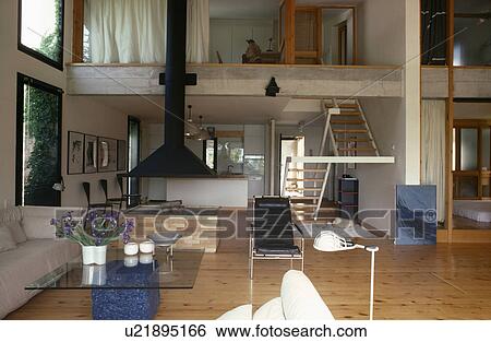 Stock Photograph - Central fireplace in openplan modern living room with mezzanine floor. Fotosearch