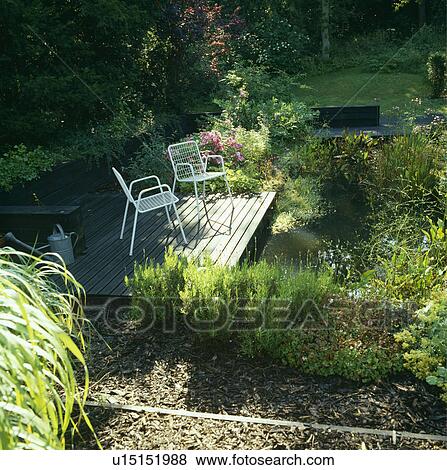 Chairs on decking beside pond in summer garden View Large Photo Image Stock Photo - Chairs on decking beside pond in summer garden. Fotosearch