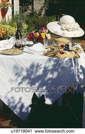Stock Image - Champagne and straw hats on garden table with white cloth. Fotosearch