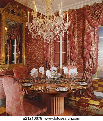 Stock Photo - Chandelier above circular table in restaurant with swagged red curtains. Fotosearch
