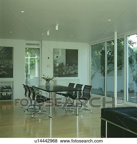 Charles Eames black leather and chrome chairs in modern dining room with wooden floor and patio doors View Large Photo Image Stock Photo - Charles Eames black leather and chrome chairs in modern dining room with wooden floor and patio doors. Fotosearch