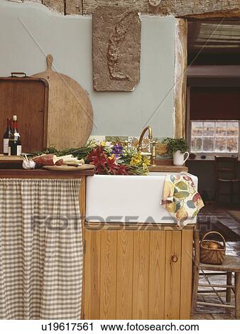 Stock Image - Checked curtain over kitchen storage beside white ceramic sink. Fotosearch