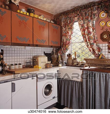 Checked curtains below sink in small kitchen with floral curtains at window stencilled terracotta fitted cupboards View Large Photo Image Stock Photograph - Checked curtains below sink in small kitchen with floral curtains at window stencilled terracotta fitted cupboards . Fotosearch
