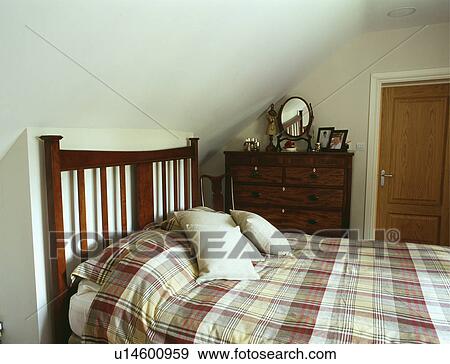Stock Photo - Checked duvet on dark wood bed in attic bedroom. Fotosearch