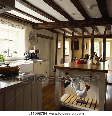 Picture - Chicken ornament on island unit in cottage kitchen with plaster removed from wall leaving exposed beams. Fotosearch