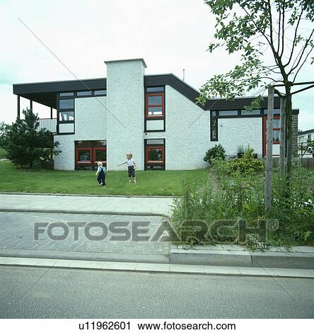 Stock Image - Children playing on lawn in front of modern white house in the country. Fotosearch
