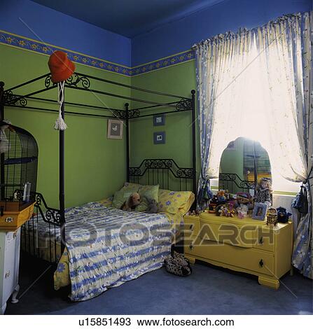 Stock Image - Child's metal four-poster bed in colourful green and blue bedroom with yellow dressing table. Fotosearch