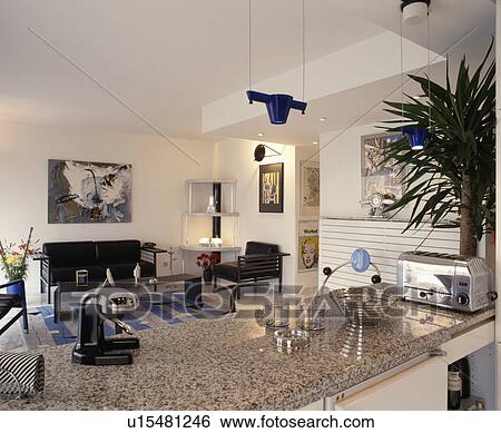 Stock Photograph - Chrome toaster and juicer on grey granite worktop in open plan modern kitchen and living room. Fotosearch