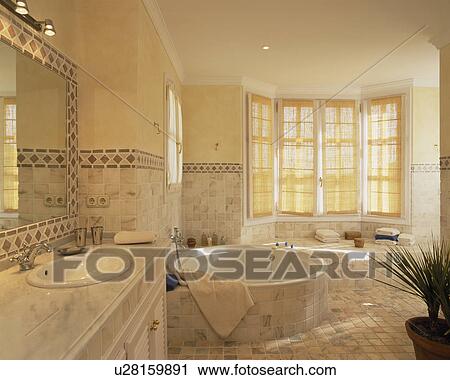 Circular bath with tiled surround in modern cream tiled bathroom with marble-topped vanity unit View Large Photo Image Stock Image - Circular bath with tiled surround in modern cream tiled bathroom with marble-topped vanity unit. Fotosearch