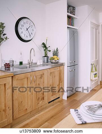 Circular clock above stainless steel sink built into wooden units in modern kitchen with fridge-freezer View Large Photo Image Stock Photo - Circular clock above stainless steel sink built into wooden units in modern kitchen with fridge-freezer. Fotosearch