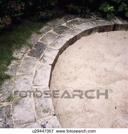 Stock Photo -  Circular sandpit with paved edging in children's play area in garden. Fotosearch