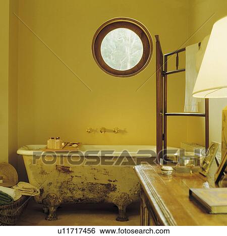 Stock Photograph - Circular window above old clawfoot bath in rustic country bathoom . Fotosearch