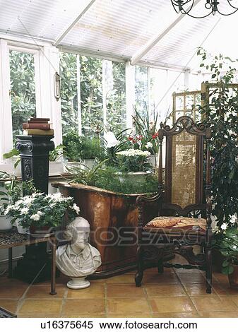 Stock Photography - Classical bust beside antique chair in conservatory in plants in old copper bath. Fotosearch
