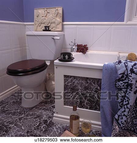 Stock Image - Classical stone plaque on toilet in blue bathroom with white tiled wall to dado height and marble-effect flooring. Fotosearch