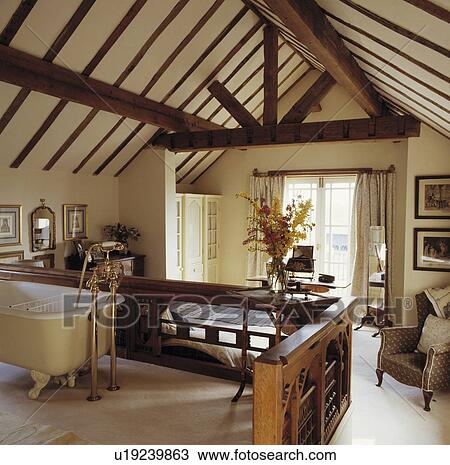 Stock Image - Clawfoot bath in openplan ensuite bathroom and bedroom with beamed apex ceiling. Fotosearch