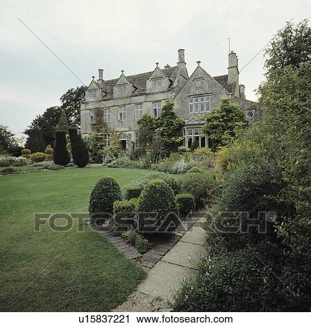 Stock Image - Clipped shrubs on lawn in front of large country house. Fotosearch